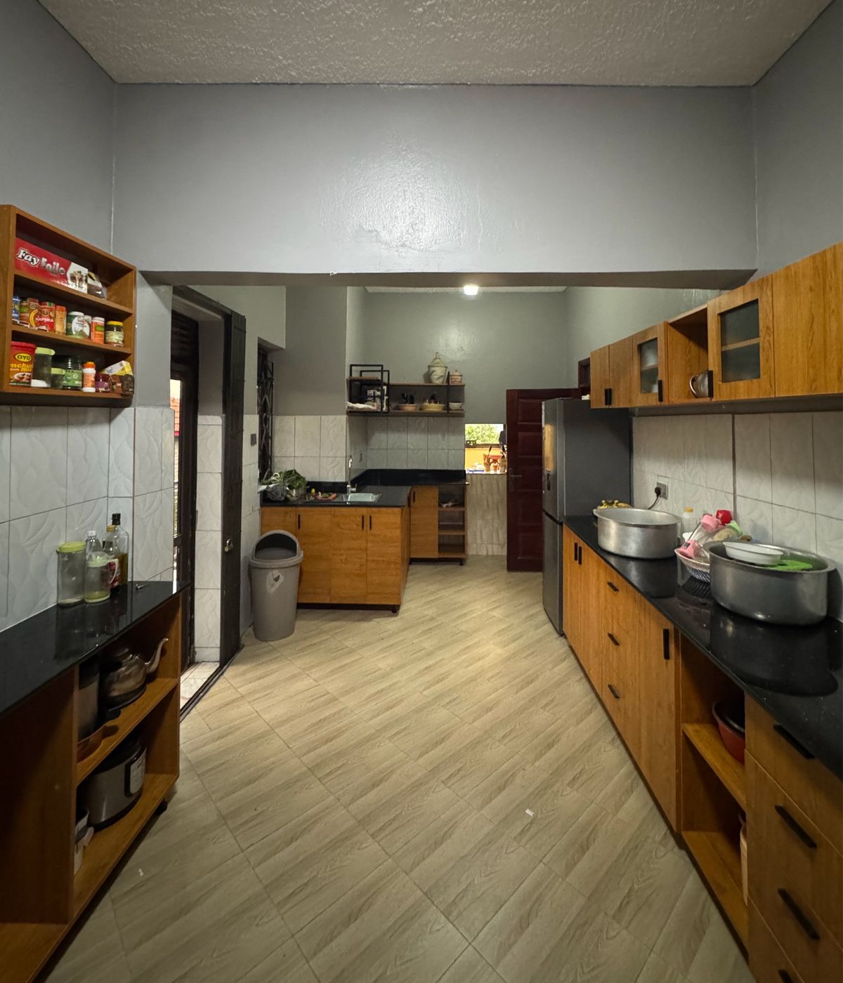The Kanyanya kitchen after the extension: a long galley with timber cabinetry, black worktops, a fridge and light wood-effect floor tiles.